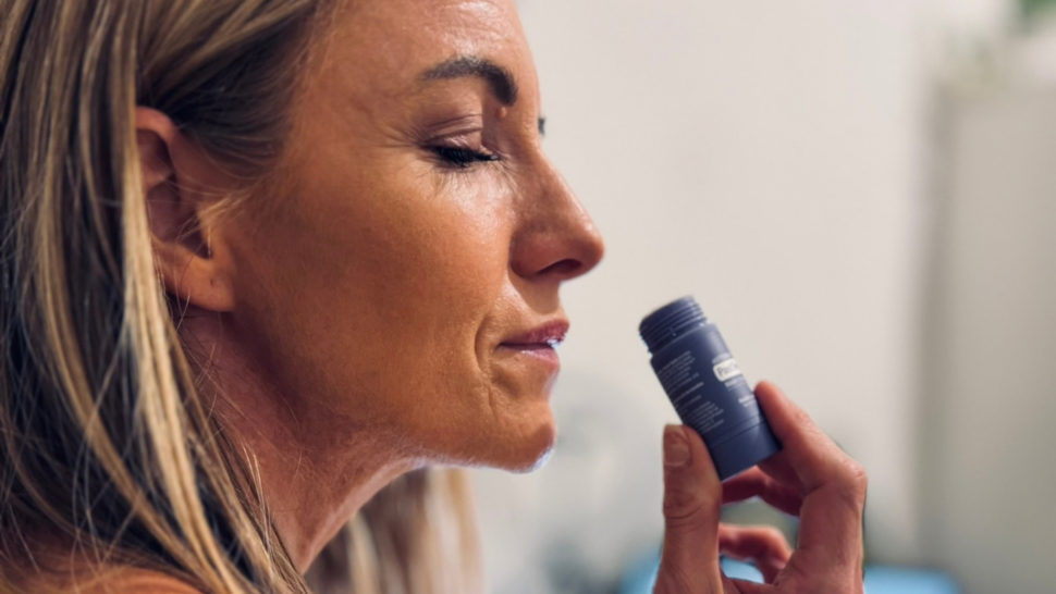 Žena so zatvorenými očami privoniava k tyčinke dōTERRA PastTense Stick Plus Sweet Gum